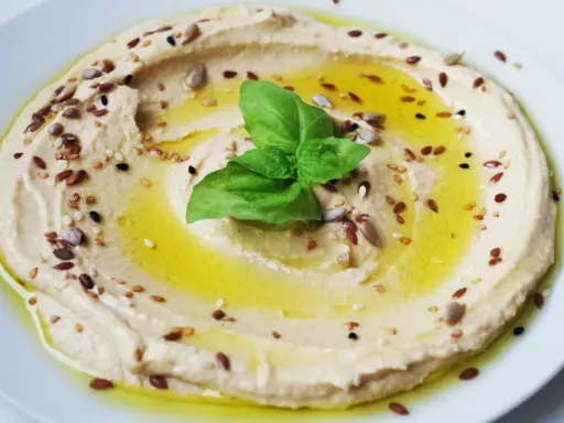 Cremiger Hummus, garniert mit Öl, Kräutern und Samen. Tahin ist die geheime Zutat für diese köstliche Dip-Kreation.