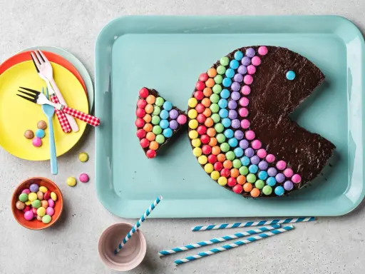 Gâteau en forme de poisson, décoré de Smarties formant un arc-en-ciel. Un œil bleu et une bouche ouverte complètent ce délice coloré.