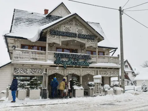 Drewniana chata z napisem "Schronisko Smaków" i neonem "Restauracja" w Bukowinie Tatrzańskiej, otoczona śniegiem.