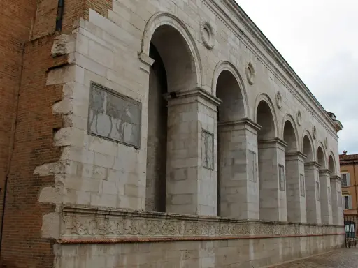 Archi maestosi e decorazioni in pietra della chiesa San Francesco a Rimini, con un muro in mattoni a vista che racconta la sua storia.