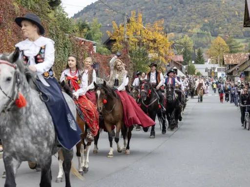 Redyk Szczawnica w barwnych strojach ludowych na koniach, w tle jesienne wzgórza i tłum widzów.
