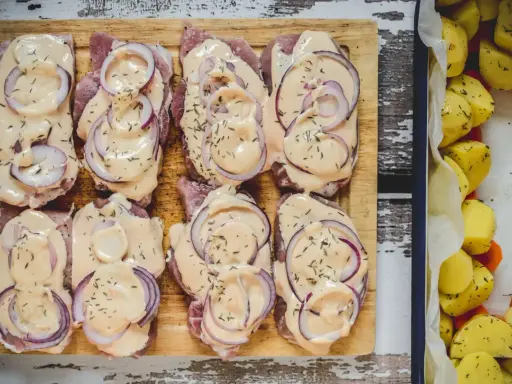 Schab pieczony w plastrach, polany kremowym sosem i posypany ziołami, obok pieczone ziemniaki.