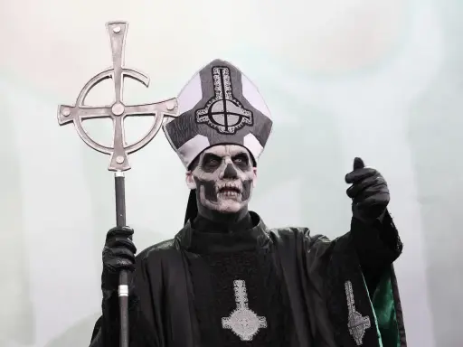 Tobias Forge som Papa Emeritus IV, med sin ikoniska sminkning och påvehatt, håller en korsstav. Han påminner om en kuslig onkel Kånkel.