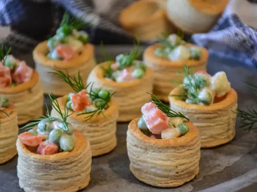 Plusieurs bouchées à la reine garnies d'une salade crémeuse de petits pois, carottes et saumon, décorées d'aneth.