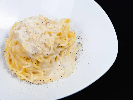 Un piatto di spaghetti cacio e pepe, cremosi e ricchi, cosparsi di pepe nero macinato fresco e formaggio grattugiato.