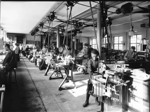 Barn arbetar vid maskiner i en verkstad, en scen från den industriella revolutionen.