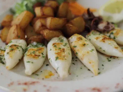 Chipirones a la plancha, tiernos y dorados, acompañados de patatas rústicas y un toque de perejil fresco.