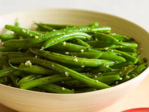 Fagiolini in padella conditi con aglio e pepe, serviti in una ciotola di legno.