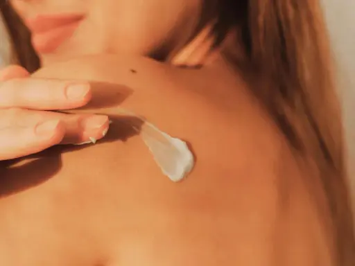 Main d'une femme appliquant une crème sur son épaule, un geste essentiel pour savoir comment bien bronzer en protégeant sa peau.