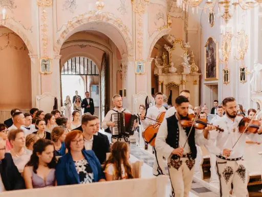 Muzycy grają piosenkę dla świadków w kościele. W tle para młoda wchodzi do świątyni.