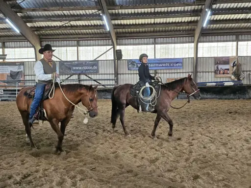Mann mit Hut und ein Jugendlicher üben Reining Reiten in einer Reithalle.