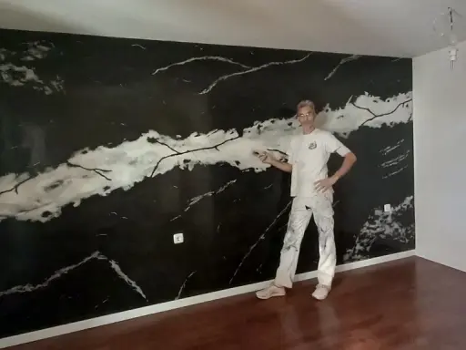 Pintor posa frente a una pared con falso estuco de mármol negro y blanco.