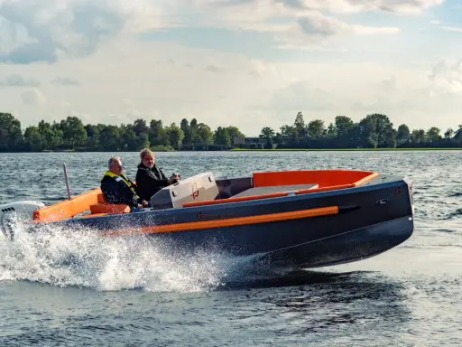 Deux hommes naviguent sur un bateau rapide, créant des éclaboussures. Le design moderne du bateau, avec ses accents orange vif, suggère une conception soignée, peut-être pour fabriquer des flaps pour bateau.