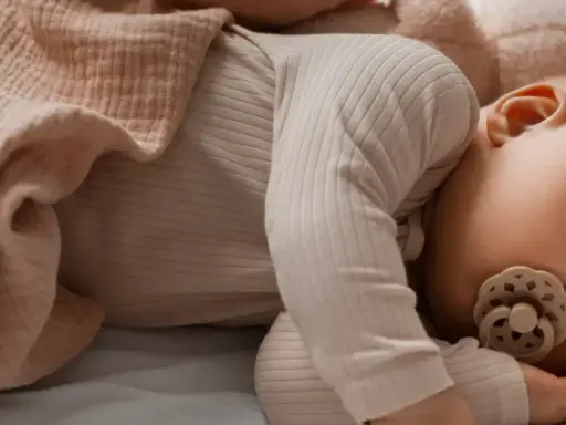 Un tenero neonato dorme sereno, avvolto in una copertina color pesca, con un ciuccio che lo culla nel sonno.