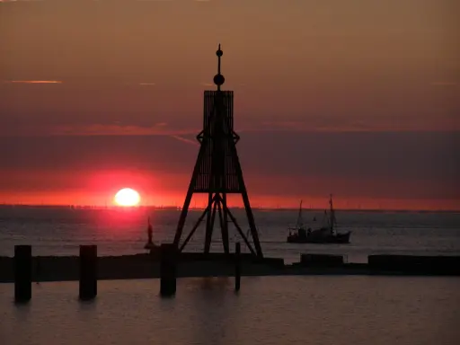 Sonnenuntergang in Cuxhaven: Ein Leuchtfeuer und ein Fischerboot auf dem Meer. Hier kann man die Weite genießen und den Tag ausklingen lassen.