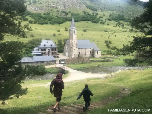 Dos niños corren por un sendero en un valle verde hacia una iglesia y casas de piedra. ¡Un plan perfecto de qué hacer en Vielha con niños!