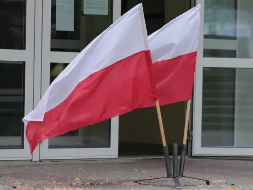 Dwa polskie flagi przed budynkiem. Dowiedz się, jak głosować za granicą, by Twój głos miał znaczenie.