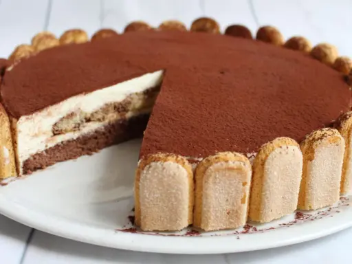 Eine köstliche tiramisu torte, mit Löffelbiskuits und Kakaopulver verziert, wartet darauf, angeschnitten zu werden.