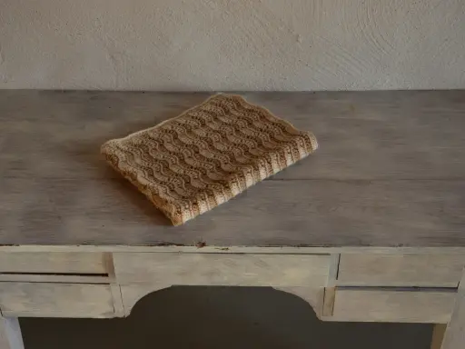 En vacker babyfilt stickad i ett vågmönster med ljusa och mörkare bruna nyanser.