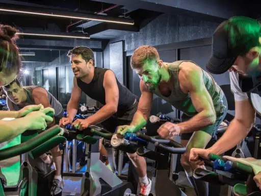 Intensywny trening spinningowy w grupie. Ludzie z determinacją pedałują na rowerach stacjonarnych, pocą się i walczą o każdy kilometr.