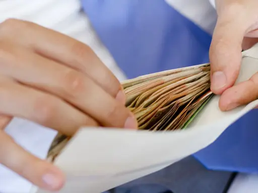Dłonie wkładają plik banknotów do koperty na wesele.