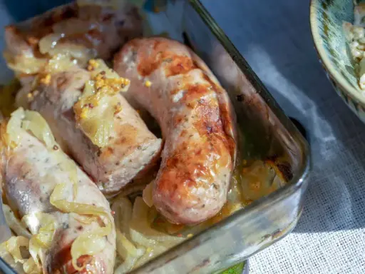 Soczysta biała kiełbasa pieczona z cebulką i musztardą, podana w szklanym naczyniu.