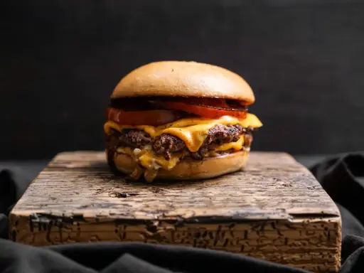 Saftiger Oklahoma Smash Burger mit geschmolzenem Käse und Tomaten auf rustikalem Holzbrett.
