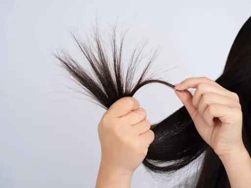 Mani che esaminano ciocche di capelli fini che si spezzano, mostrando la fragilità e la necessità di cura.