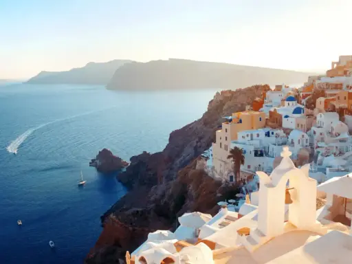 Traumhafter Blick auf die weißen Häuser und blauen Kuppeln von Santorini. Das Meer glitzert, Boote fahren vorbei. Ein perfekter Santorini Strand Urlaub.