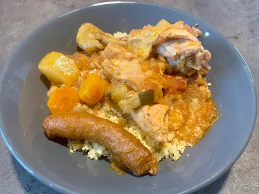 Un plat appétissant de tajine poulet merguez, servi sur un lit de semoule, avec des morceaux de poulet, des légumes et une merguez dorée.