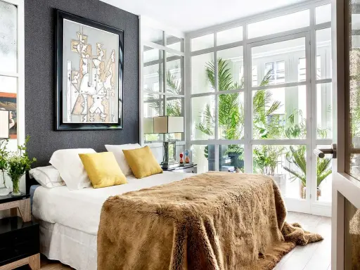 Un dormitorio moderno con cama mullida, arte abstracto y ventanales que invitan a diseña tu dormitorio con luz natural y plantas.