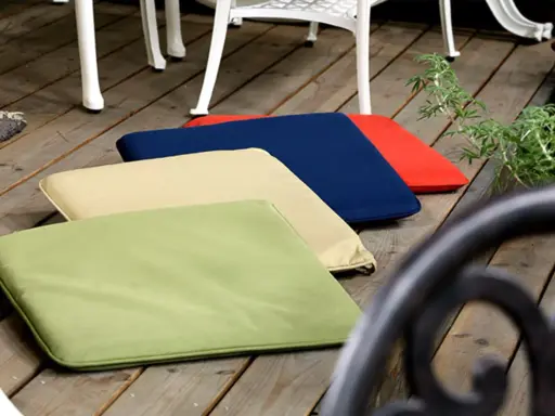 Mehrere bunte gartenpolster nass geworden, liegen auf einer Holzterrasse neben Gartenmöbeln.