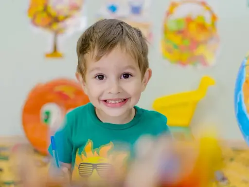 Niño sonriente con camiseta verde, rodeado de materiales educativos. Fomenta la autoestima en niños.