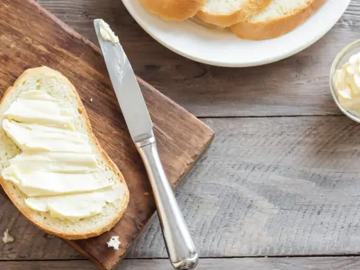 Brot mit Butter bestrichen, daneben eine Schale mit Butter und ein Messer. Ob Butter oder Margarine, beides enthält Cholesterin.
