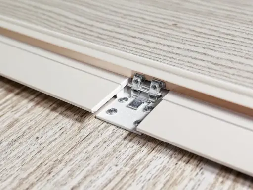 Détail d'une lame PVC qui se soulève, révélant une fixation métallique et des vis sur un parquet imitation bois.