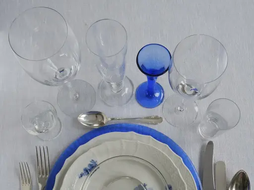 Vacker dukning med flera glas, tallrikar och bestick. En blå glaskupa sticker ut.