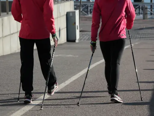 Dwie osoby w czerwonych kurtkach i czarnych spodniach maszerują z kijki do nordic walking.