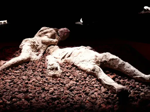 Pompeje zastygli ludzie w popiele, ostatnie chwile uwiecznione w kamieniu. Dwie postacie leżą obok siebie, otoczone gruzem.