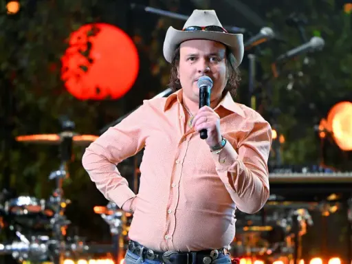 David Ritschard konsert. Artist med cowboyhatt och orange mönstrad skjorta sjunger i mikrofon på scenen.