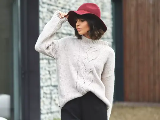Elegancka kobieta w bordowym kapeluszu i beżowym swetrze z warkoczami. Stylowe sukienka i sweter stylizacje na chłodniejsze dni.