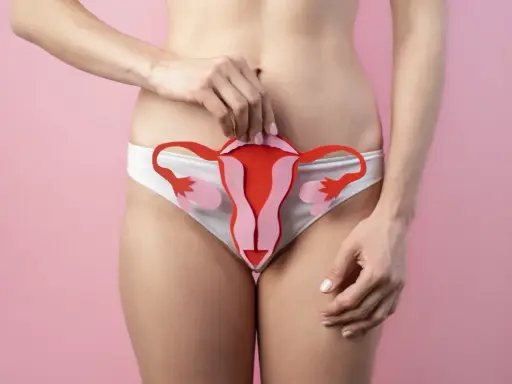 Kobieta trzyma wycięty z papieru model narządów rodnych na tle w kolorze różowym.