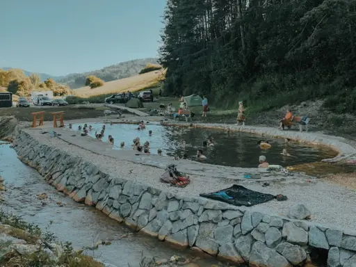 Relaks w gorących źródłach na Słowacji blisko granicy. Ludzie kąpią się w naturalnym basenie, otoczonym kamieniami i zielenią.