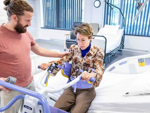 Un homme aide une femme à s'asseoir sur un lève-personne, illustrant l'ergonomie infirmier pour un transfert sécurisé.