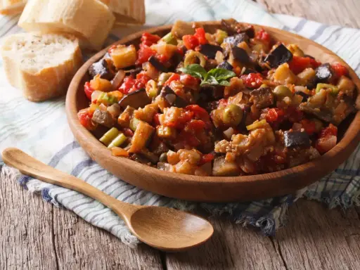 Un plat de caponata, une recette sicilienne savoureuse, garni de basilic frais, servi avec du pain croustillant.
