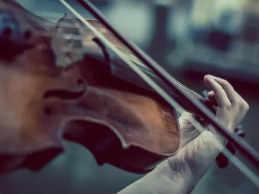 Main d'un musicien jouant du violon, un instrument à cordes, pas à vent. La musique s'élève.