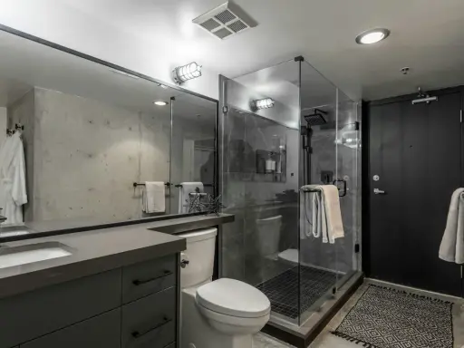 Baño moderno con mampara de ducha de cristal, inodoro, lavabo y puerta negra. Varios tipos de mamparas de ducha se ven en la imagen.