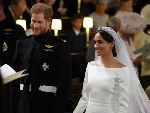 Meghan Markle y el Príncipe Harry sonríen en su boda. Ella luce un vestido blanco y él un uniforme militar.