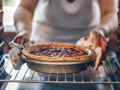 Hände mit Ofenhandschuhen nehmen einen frisch gebackenen Nusskuchen aus dem Ofen. Alles, was man zum Backen braucht: Zutaten, ein Rezept und Geduld.