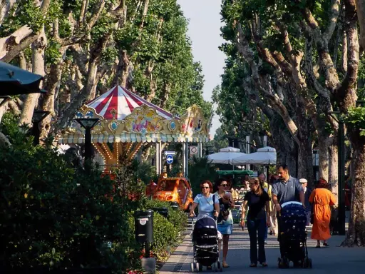Passeggiata nel centro di Bellaria, con giostra, alberi maestosi e famiglie con passeggini.