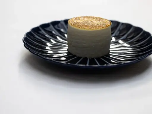 Un cylindre blanc, saupoudré d'or, sur une assiette bleue. Une idée de quoi manger à Paris pour une expérience culinaire unique.